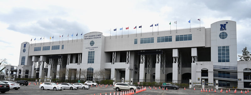 The north facade of Navy-Marine Corps Memorial Stadium in Annapolis, with flags along the roofline and the stadium lot in front