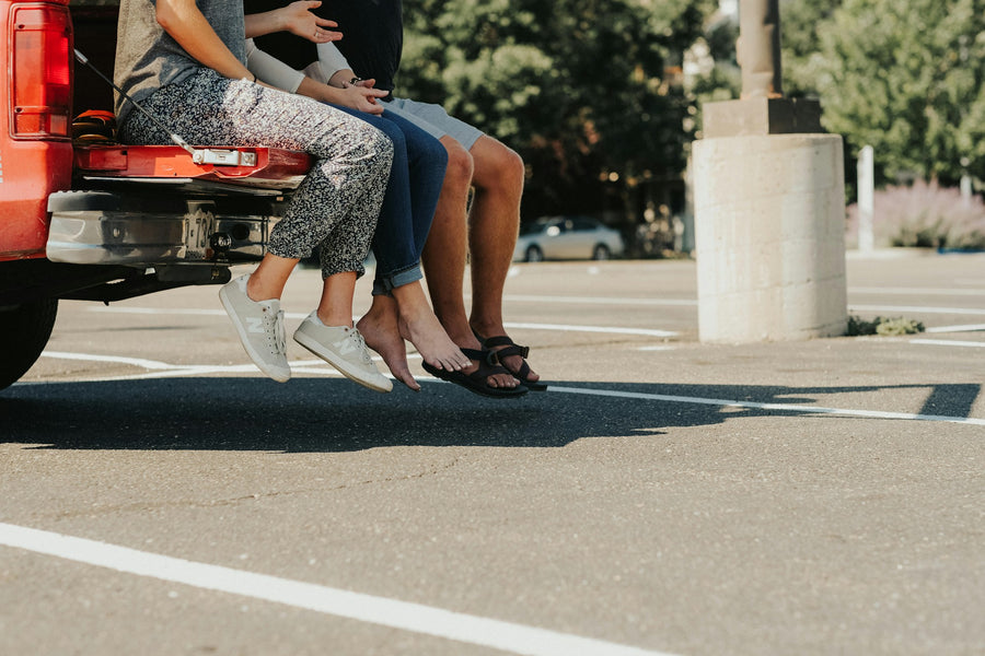 Three friends sitting on a red pickup tailgate in a parking lot, feet dangling
