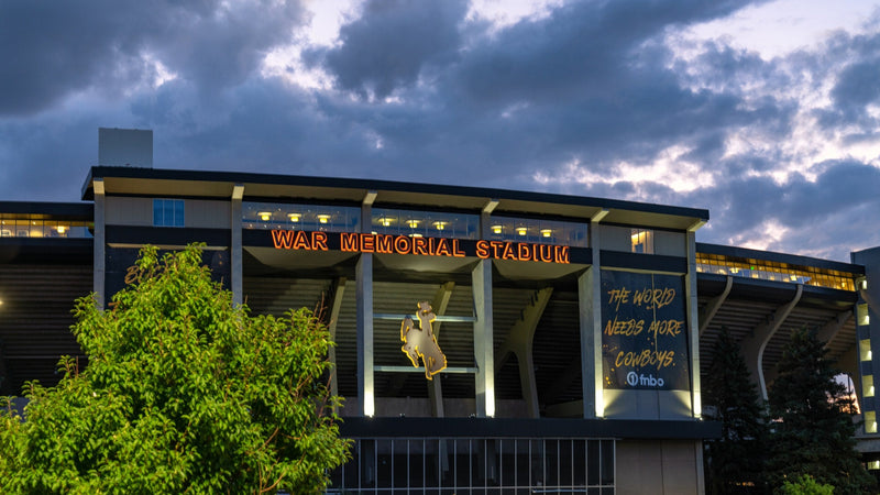War Memorial Stadium in Laramie at dusk, its name lit in orange across the facade