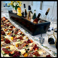 Load image into Gallery viewer, Black three-section cooler holding wine and juice on ice behind a long spread of charcuterie boards