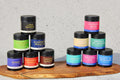 Load image into Gallery viewer, Pyramid of World Spice tins in assorted colors, other blends from the same company, on a wooden board