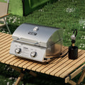 Load image into Gallery viewer, Closed tabletop grill on a slatted camp table, hooked to a 1 lb propane cylinder