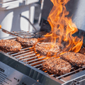 Load image into Gallery viewer, Flames rising around burgers as a spatula flips one on the grill grates