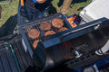 Load image into Gallery viewer, Burgers on an open tabletop grill on a lowered tailgate, cooler and condiments beside it