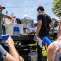 Load image into Gallery viewer, Friends with red cups and a cooler at a pickup tailgate while one tends the grill on a 20 lb tank