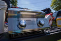 Load image into Gallery viewer, Closed grill sitting on a pickup tailgate next to a cooler and a bag of chips