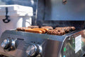 Load image into Gallery viewer, Burgers and hot dogs on the grill in a truck bed, lid open, cooler behind