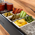 Load image into Gallery viewer, Close-up of Bloody Mary garnish trays: olives, pickled green beans, bacon, celery, lemon and lime wedges beside ice