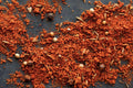 Load image into Gallery viewer, Coarse red-orange barbecue rub scattered on a dark slate with whole allspice, cumin seeds and peppercorns
