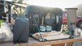 Load image into Gallery viewer, Open camp kitchen bag on a picnic table with the bamboo board folded out, mugs, plates and bread, a camper van behind