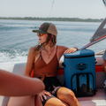 Load image into Gallery viewer, Woman in sunglasses on a moving boat, resting a hand on a blue backpack cooler beside her seat