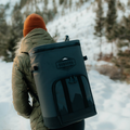 Load image into Gallery viewer, Woman in a winter jacket and knit hat wearing a backpack cooler on a snowy trail
