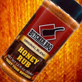 Load image into Gallery viewer, Close-up of the Honey Rub shaker label at an angle over a honeycomb background