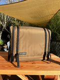 Load image into Gallery viewer, Closed brown kitchen bag on a wooden picnic table under a tan shade sail
