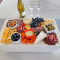 Load image into Gallery viewer, Full charcuterie board covering a white cooler on a marble island, with white wine and two gold-rim glasses