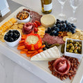 Load image into Gallery viewer, Overhead of a charcuterie spread on white boards over a cooler: brie, salami roses, olives, grapes, almonds