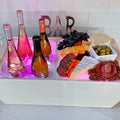 Load image into Gallery viewer, White cooler glowing pink with wine bottles on ice and a cheese, salami and olive board, BAR letters behind