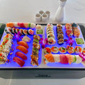 Load image into Gallery viewer, Sushi platter on white boards lit blue from below by light-up cubes in the ice, sake set behind