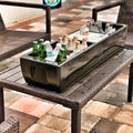 Load image into Gallery viewer, Long black cooler on a wicker patio table filled with beer and water bottles on ice, with a condiment tray in the middle