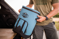 Load image into Gallery viewer, Man lifting a slate-blue backpack cooler by its side handle out of a vehicle