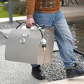 Load image into Gallery viewer, Man carrying the closed grill by its top handle along a gravel path, hose and regulator attached