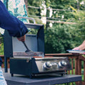 Load image into Gallery viewer, Two people at a deck table, one sliding a spatula under burgers on the open grill