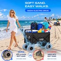 Load image into Gallery viewer, Woman walking beside the loaded electric wagon on a beach while a man in the background drags a narrow-wheeled wagon