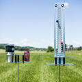 Load image into Gallery viewer, Scorezit score tower with red and blue knobs on one stake and a Drinkit holding a tumbler and soda can on another, in a field