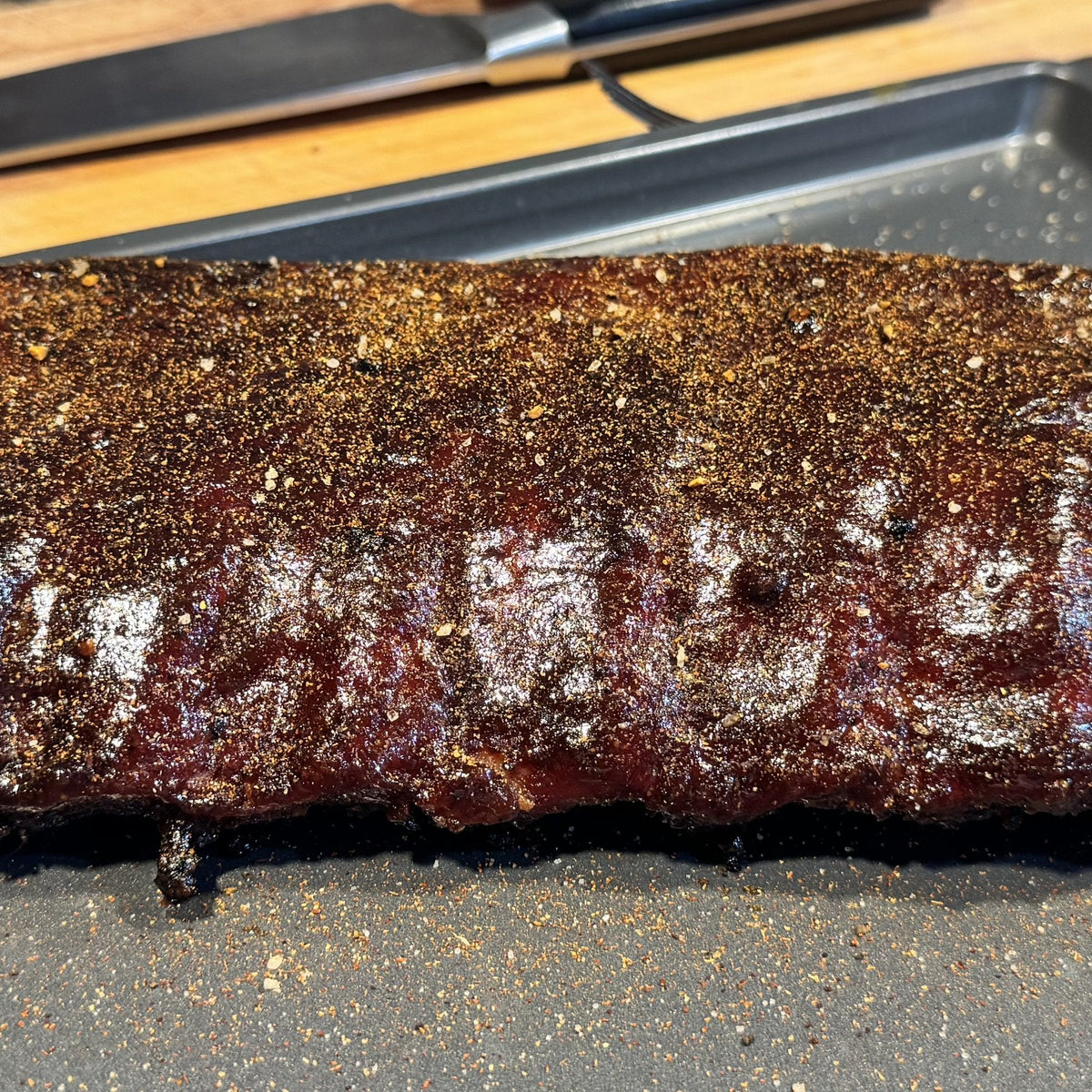A rack of smoked baby back ribs with a glossy glaze and a dusting of rub on a sheet pan