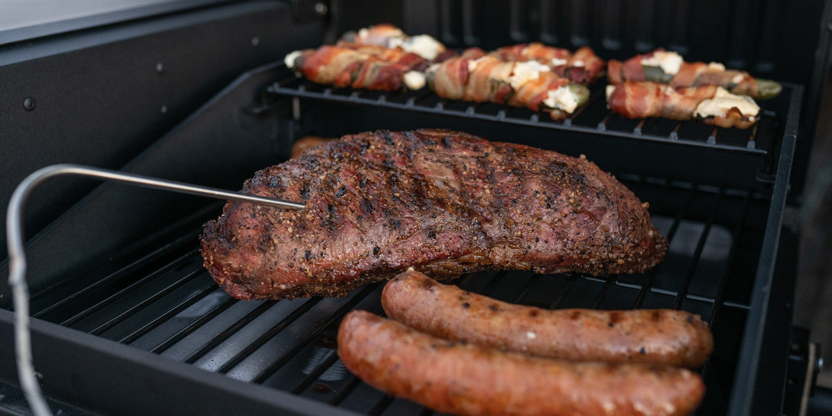 Steak, sausages and bacon-wrapped peppers on a grill set up in a truck bed