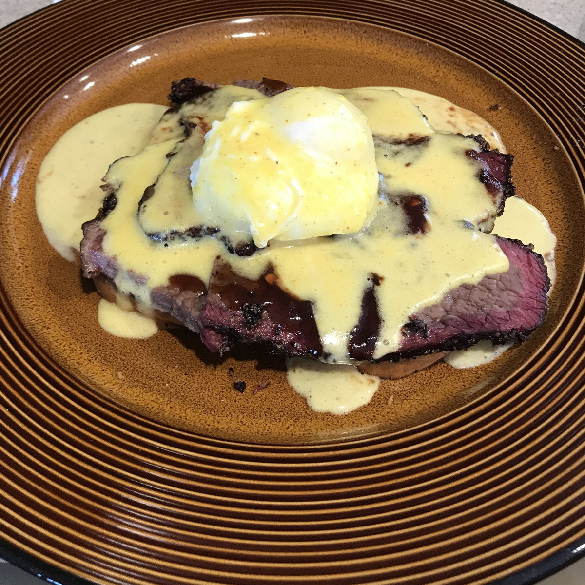 Brisket eggs Benedict: a poached egg and hollandaise over sliced smoked brisket on a plate