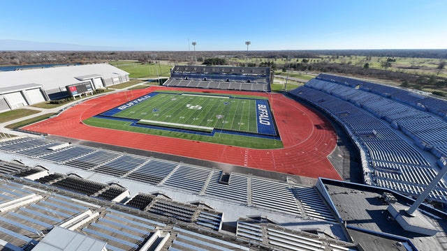 The UB football stadium in Amherst seen from high above the stands, with the blue end zones, red track and flat land beyond