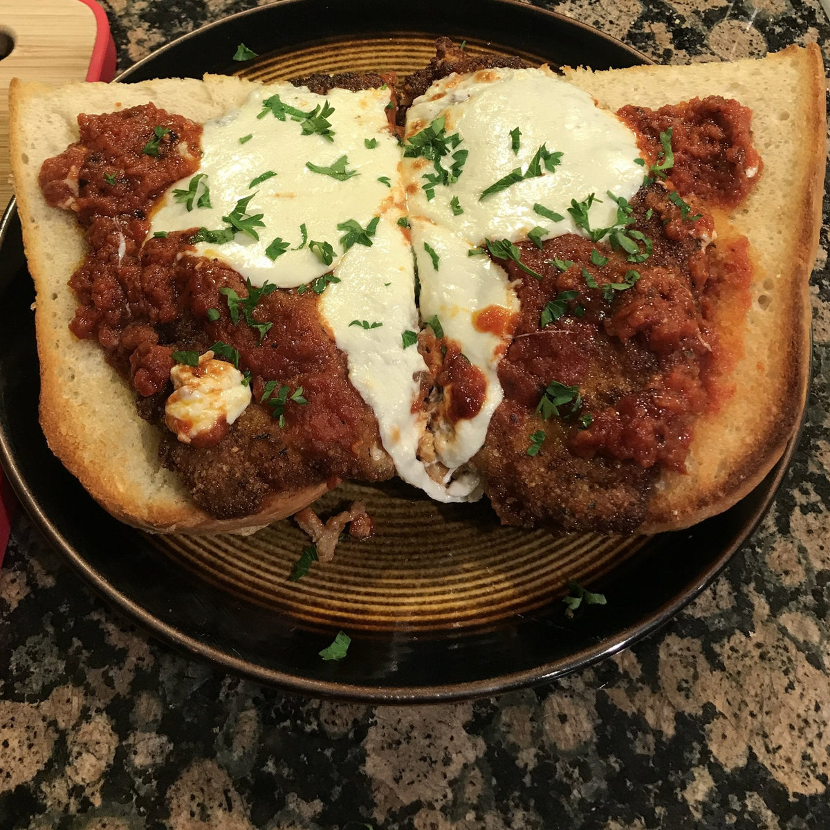 A chicken parm sub on a long toasted loaf, breaded cutlets under red sauce and melted mozzarella