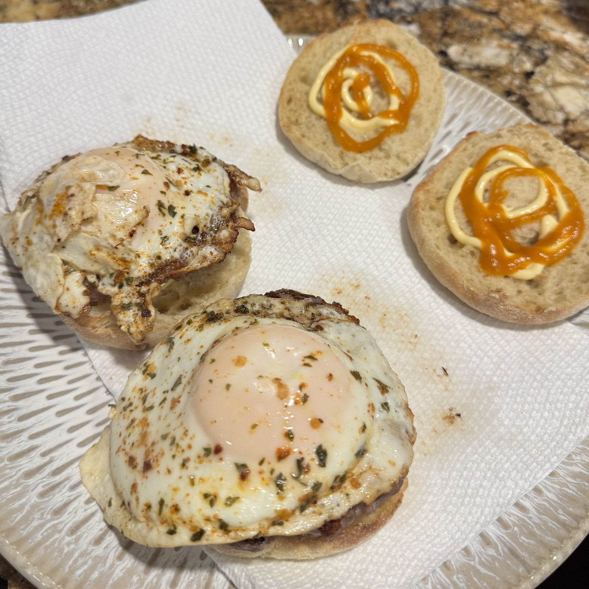 Two ham and egg breakfast sandwiches on toasted English muffins with mayo and sriracha