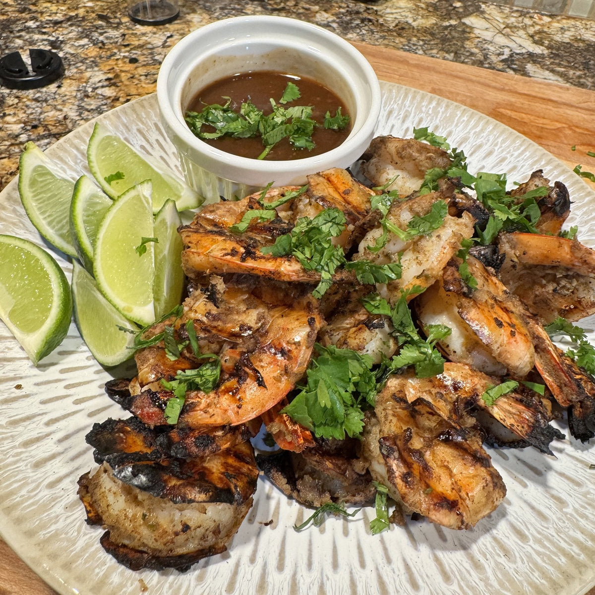 Grilled shell-on jerk shrimp split down the back, with cilantro, lime wedges and a ramekin of dipping sauce