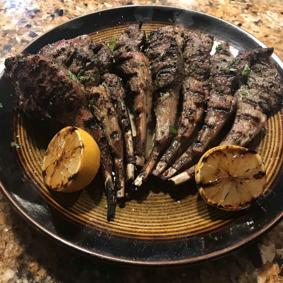 Grilled lamb lollipops with char and herbs, fanned on a plate with lemon halves