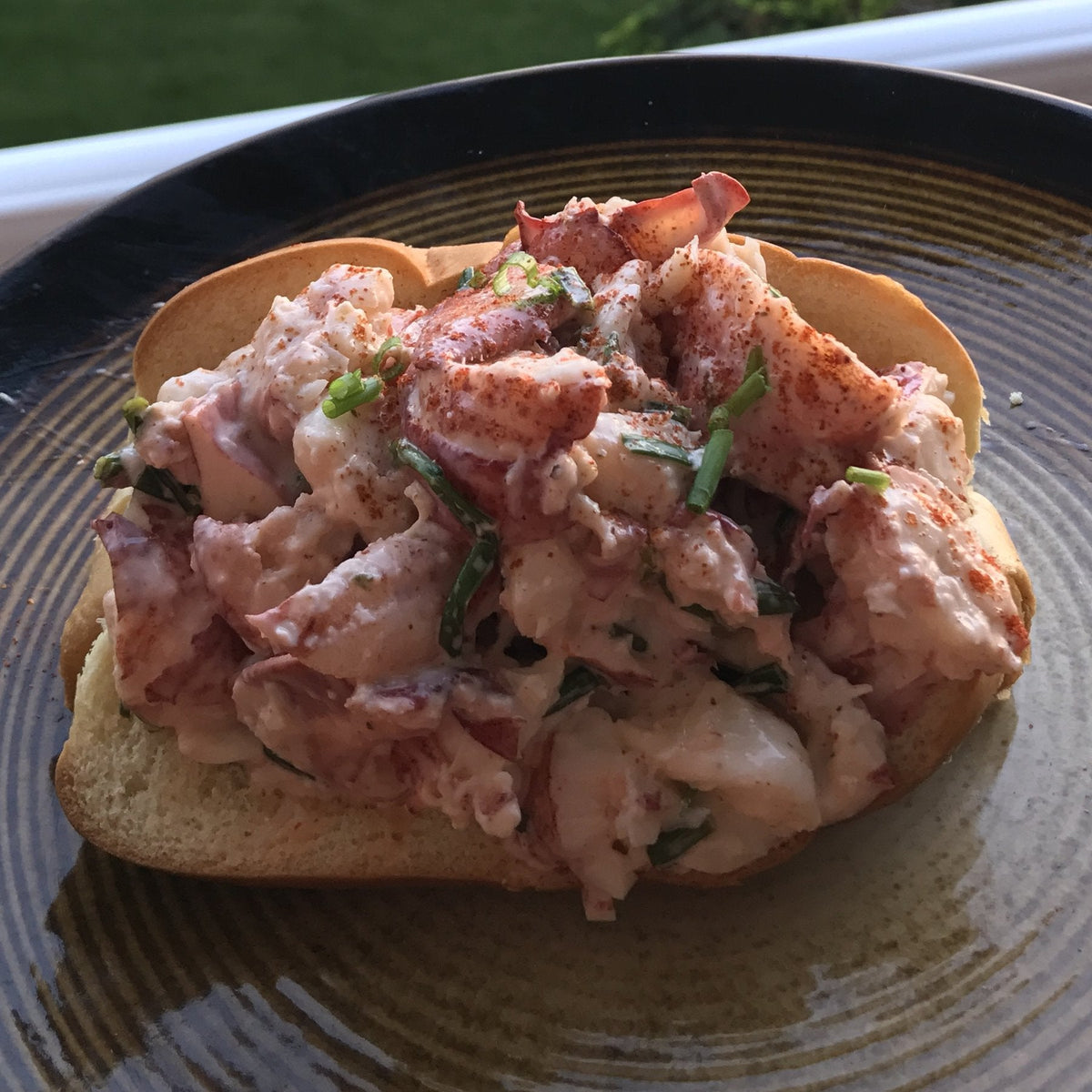A Maine lobster roll heaped with chunky lobster salad, chives and paprika in a toasted split-top bun