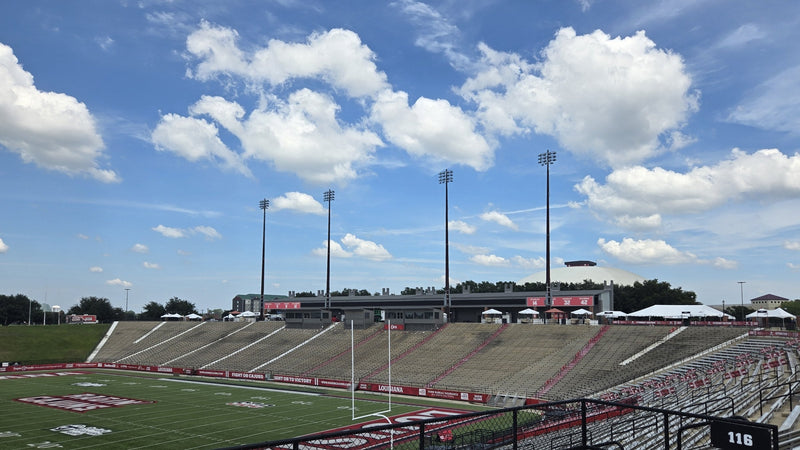 Inside Our Lady of Lourdes Stadium in Lafayette on a sunny afternoon, looking across the field to the stands and tailgate tents