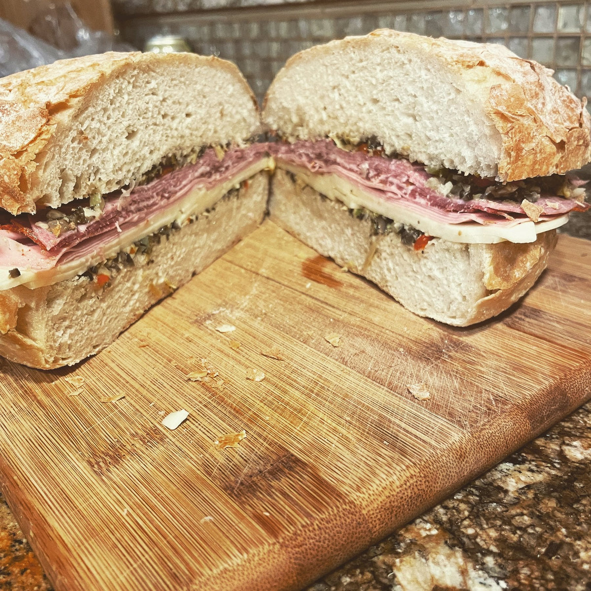 A muffuletta cut in half on a cutting board, layered with cured meats, provolone and olive salad