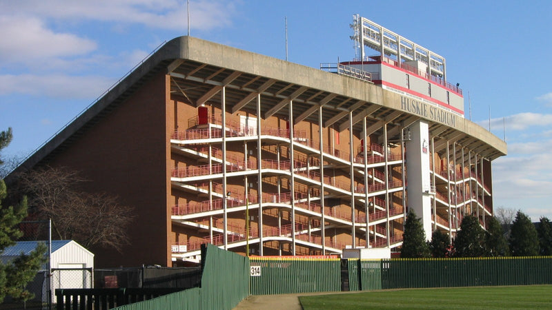 The brick and concrete west grandstand of Huskie Stadium in DeKalb under a blue sky