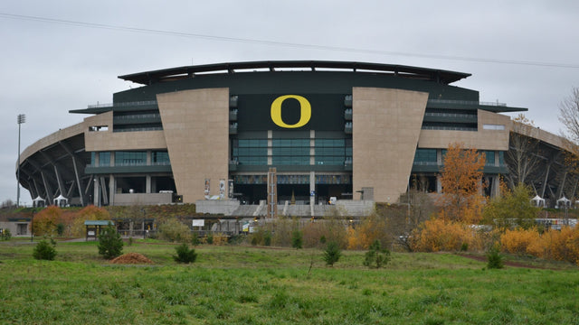 The tan and green facade of Autzen Stadium in Eugene, with fall trees in front