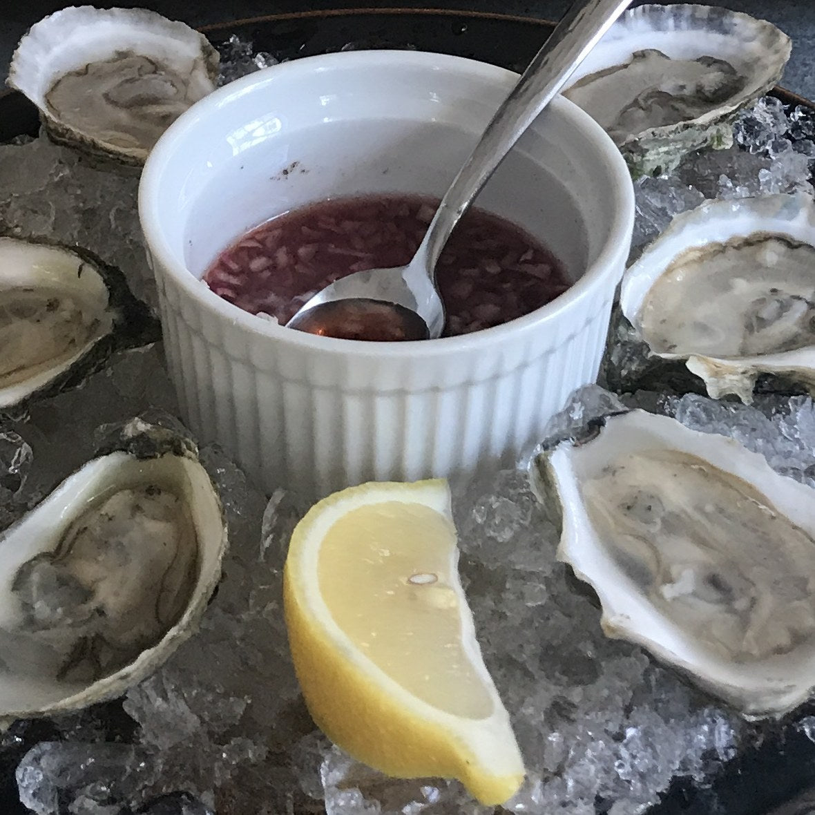 Raw oysters on the half shell over crushed ice, with a ramekin of mignonette and a lemon