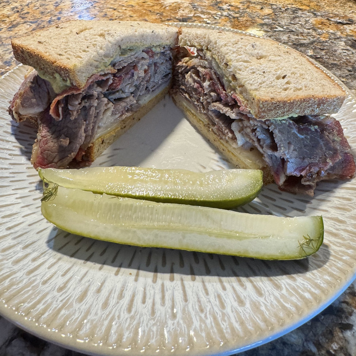A pastrami on rye sandwich cut in half, piled thick, with two pickle spears on the plate