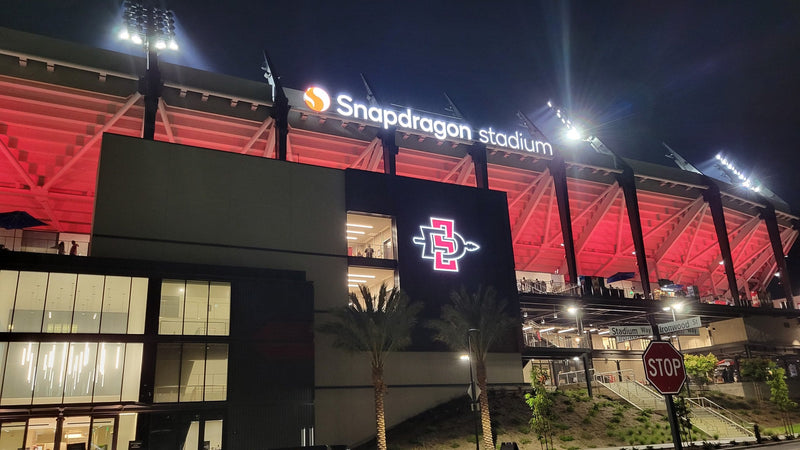 Snapdragon Stadium lit up at night in Mission Valley, San Diego, with its name on the roofline
