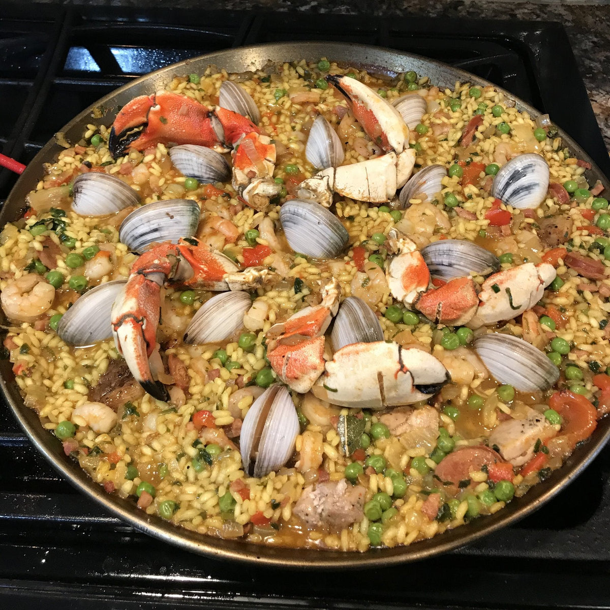 A wide pan of seafood paella with saffron rice, clams, crab, shrimp, chicken and chorizo