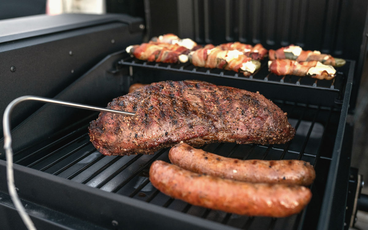 Tri-tip with a probe thermometer, sausages and stuffed peppers on a grill in a truck bed
