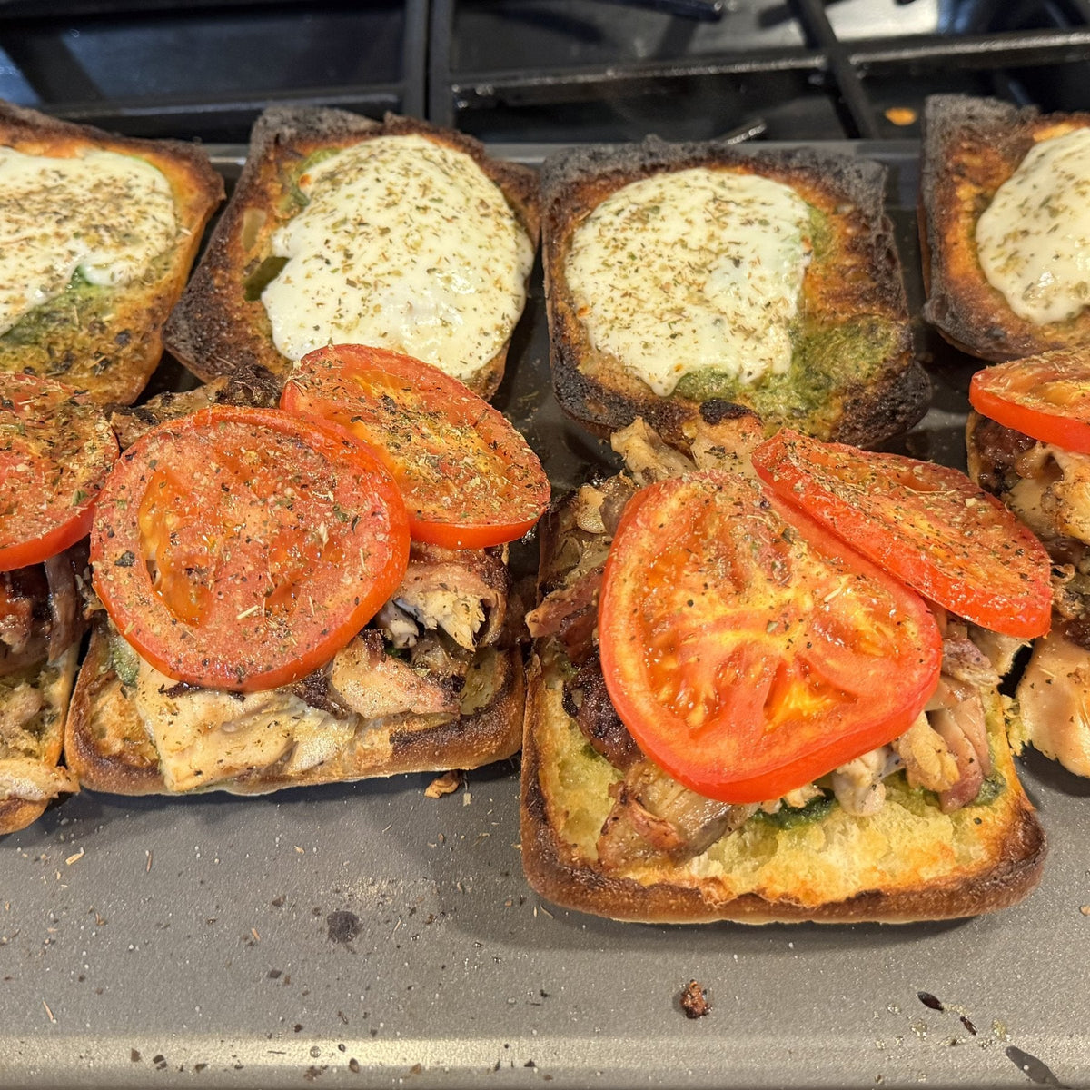 Open-faced turkey pesto sandwiches on toasted ciabatta with melted cheese and tomato on a sheet pan