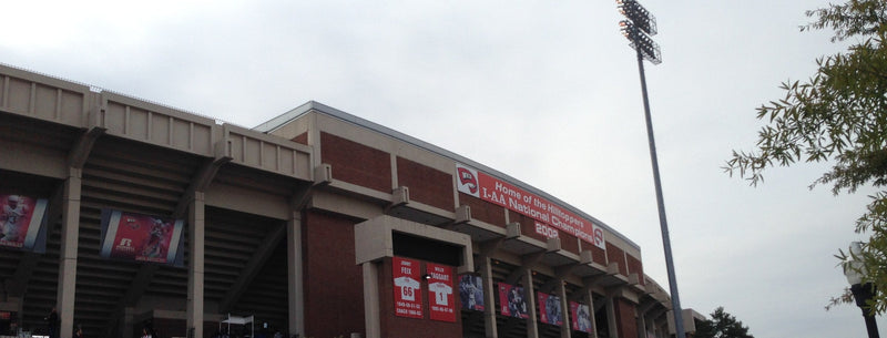 The brick and concrete exterior of Houchens-Smith Stadium in Bowling Green, with red banners and a light tower