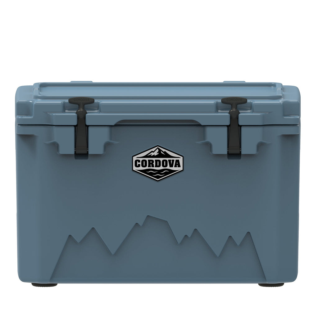 Slate-blue hard cooler from the front, two black rubber latches, a Cordova badge and a mountain graphic
