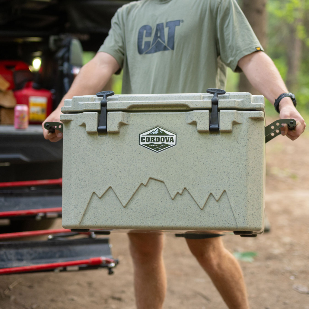 Close-up of a man holding a tan hard cooler by both handles in front of a truck bed